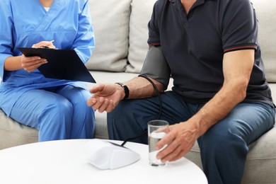 Photo of Nurse measuring senior man's blood pressure and writing results at home, closeup