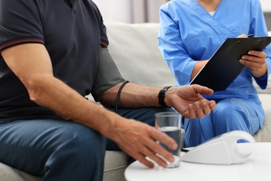 Photo of Nurse measuring senior man's blood pressure and writing results at home, closeup