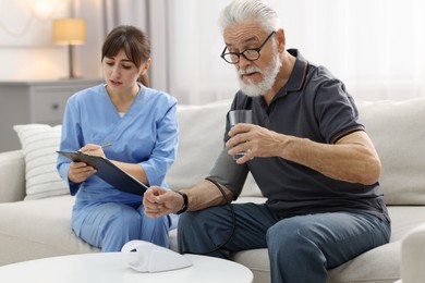 Photo of Nurse measuring senior man's blood pressure and writing results at home