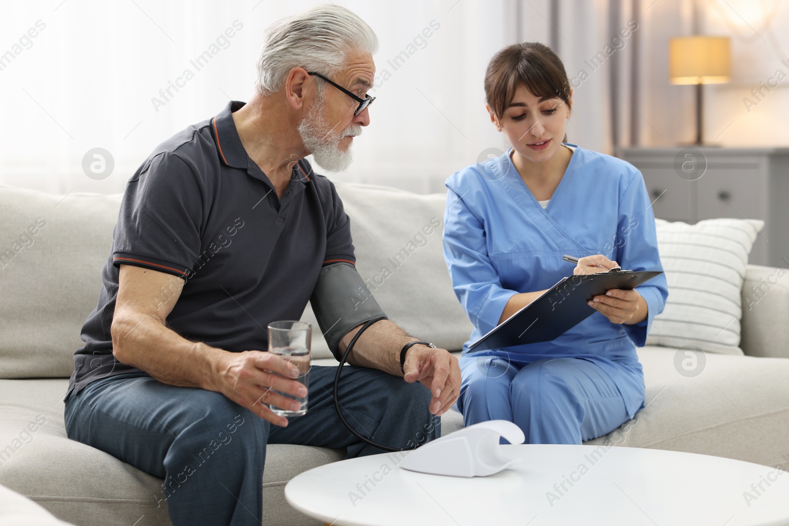 Photo of Nurse measuring senior man's blood pressure and writing results at home