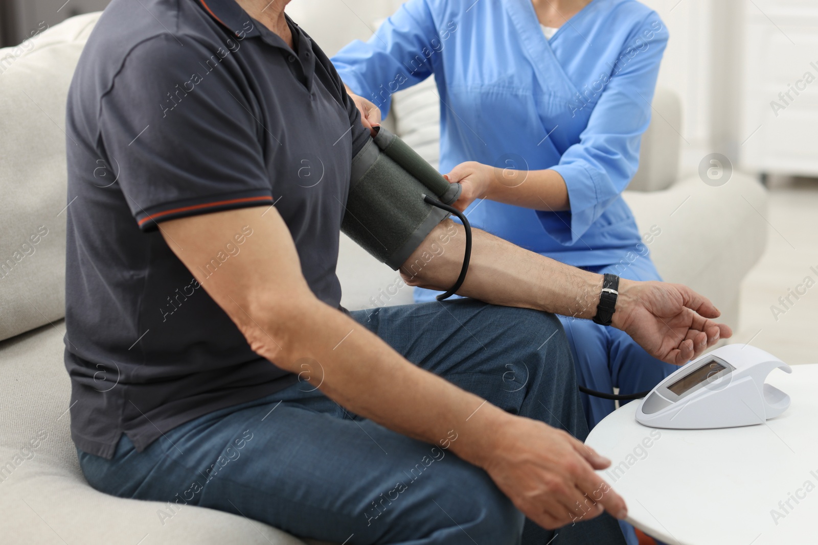 Photo of Nurse measuring senior man's blood pressure at home, closeup