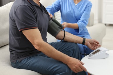 Photo of Nurse measuring senior man's blood pressure at home, closeup