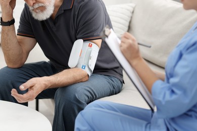 Photo of Nurse measuring senior man's blood pressure and writing results at home, closeup