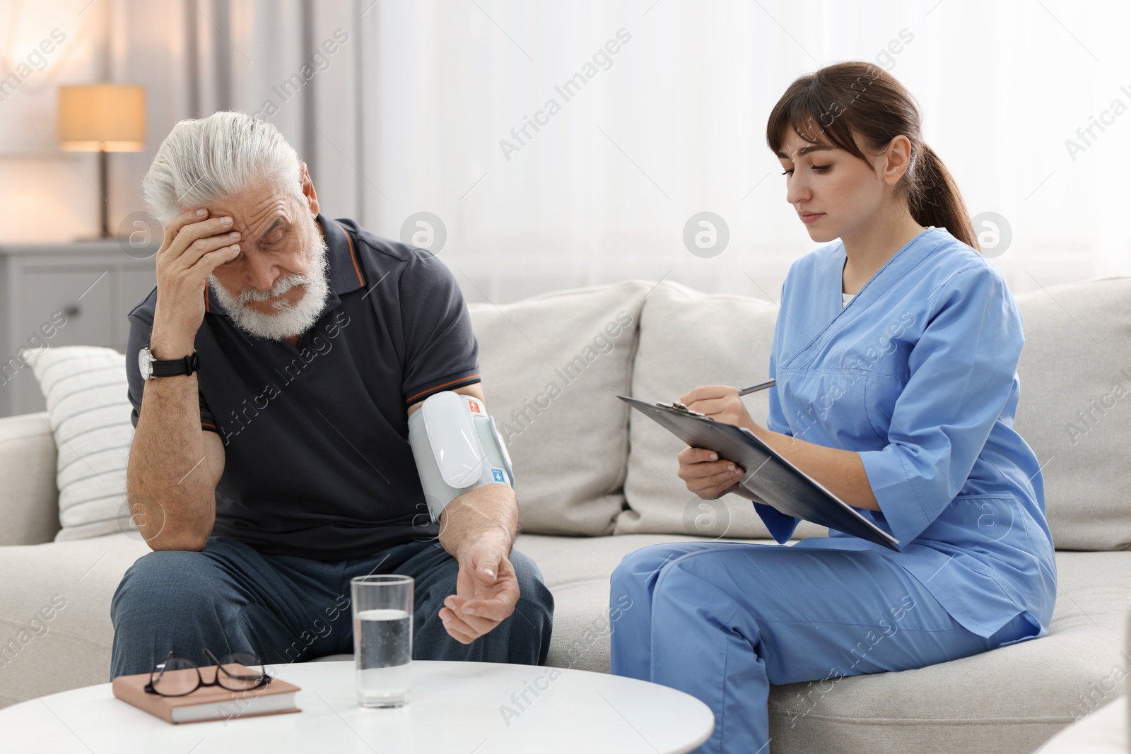 Photo of Nurse measuring senior man's blood pressure and writing results at home