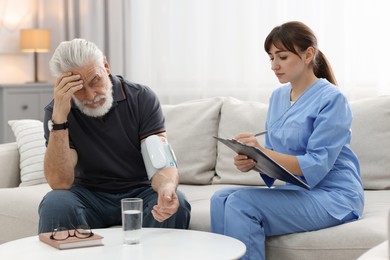 Photo of Nurse measuring senior man's blood pressure and writing results at home