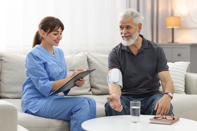 Photo of Nurse measuring senior man's blood pressure and writing results at home