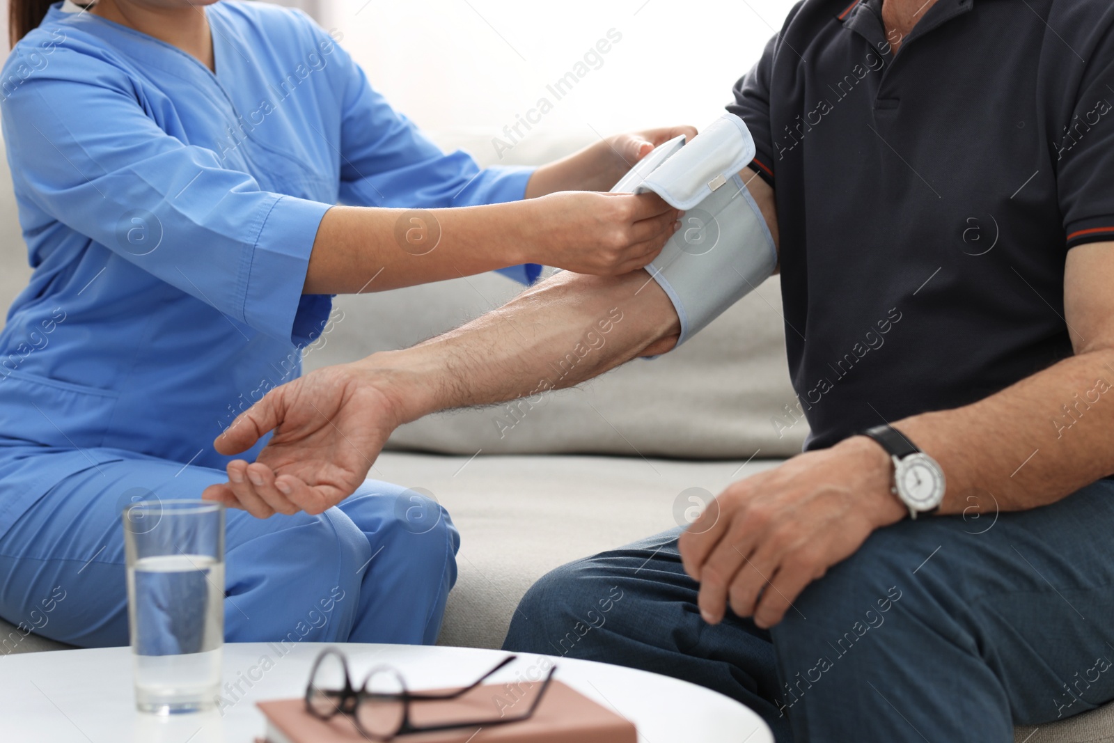 Photo of Nurse measuring senior man's blood pressure at home, closeup