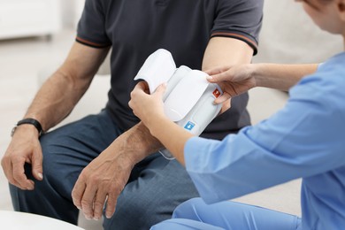 Nurse measuring senior man's blood pressure at home, closeup