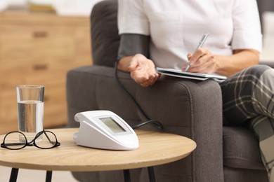 Photo of Senior woman writing results of blood pressure measurement at home, closeup