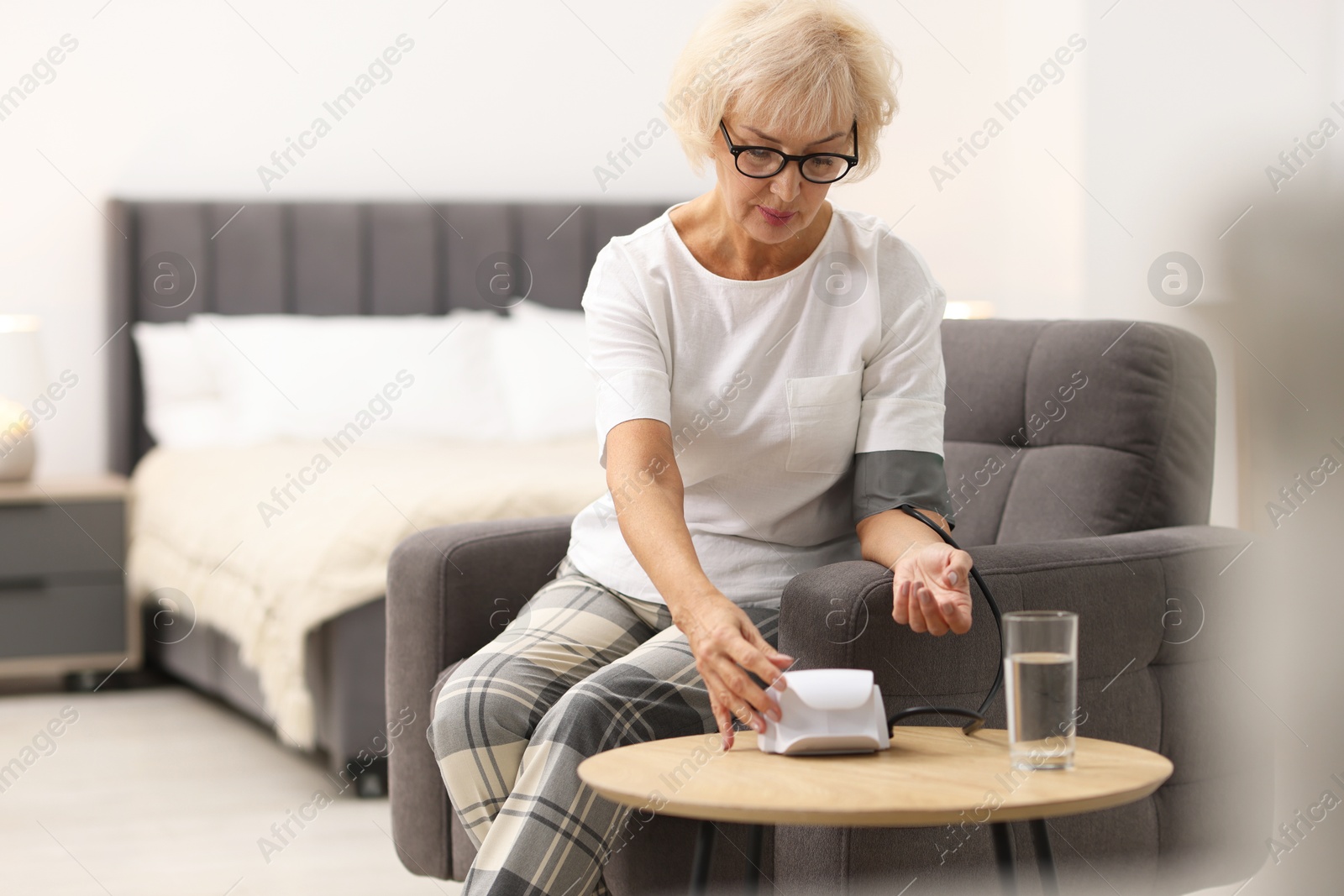 Photo of Senior woman measuring blood pressure in armchair at home