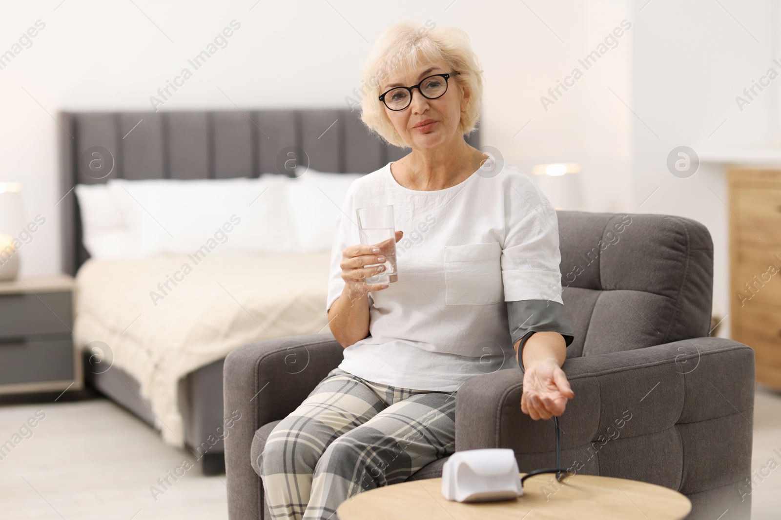 Photo of Senior woman measuring blood pressure in armchair at home