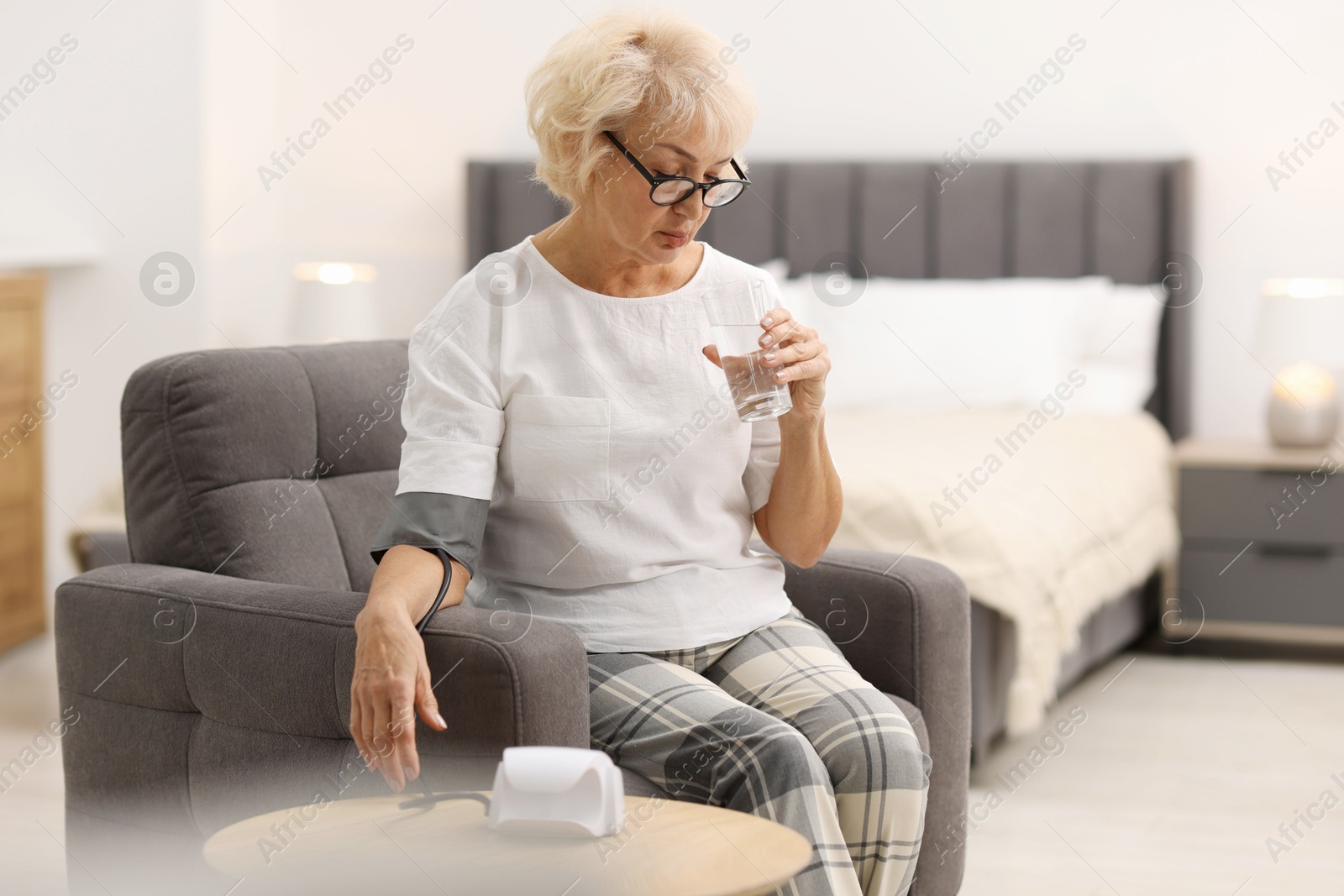 Photo of Senior woman measuring blood pressure in armchair at home