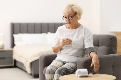 Photo of Senior woman measuring blood pressure in armchair at home. Space for text