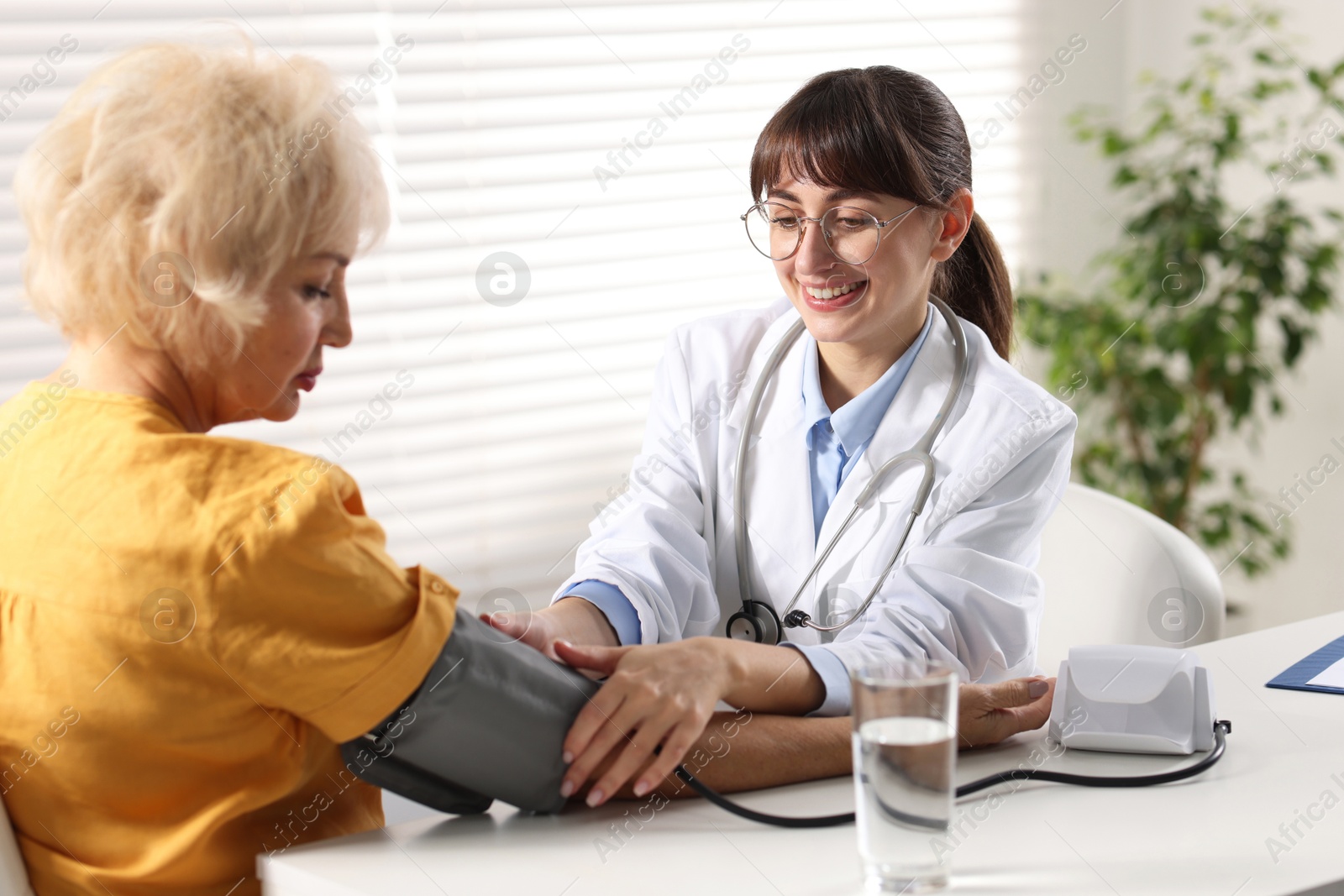 Photo of Doctor measuring senior woman's blood pressure during appointment in hospital