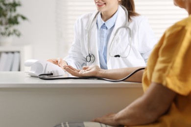 Doctor measuring senior woman's blood pressure during appointment in hospital, closeup