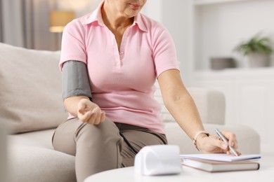 Photo of Senior woman writing results of blood pressure measurement at home, closeup