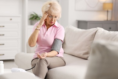 Photo of Senior woman measuring blood pressure on sofa at home