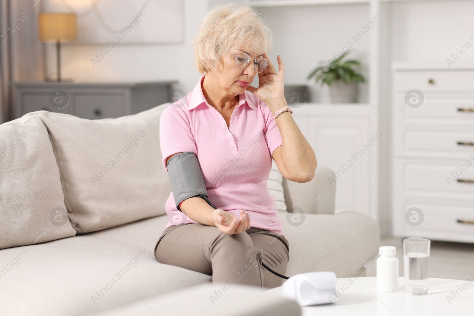 Photo of Senior woman measuring blood pressure on sofa at home