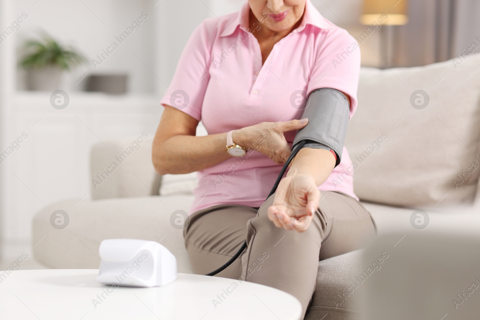 Photo of Senior woman measuring blood pressure on sofa at home, closeup