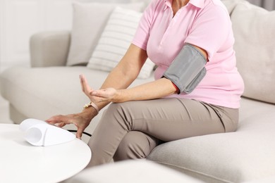 Photo of Senior woman measuring blood pressure on sofa at home, closeup