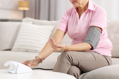 Photo of Senior woman measuring blood pressure on sofa at home, closeup