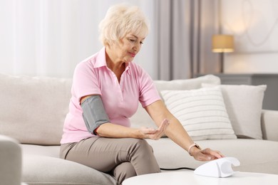 Photo of Senior woman measuring blood pressure on sofa at home