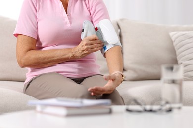 Photo of Senior woman measuring blood pressure on sofa at home, closeup