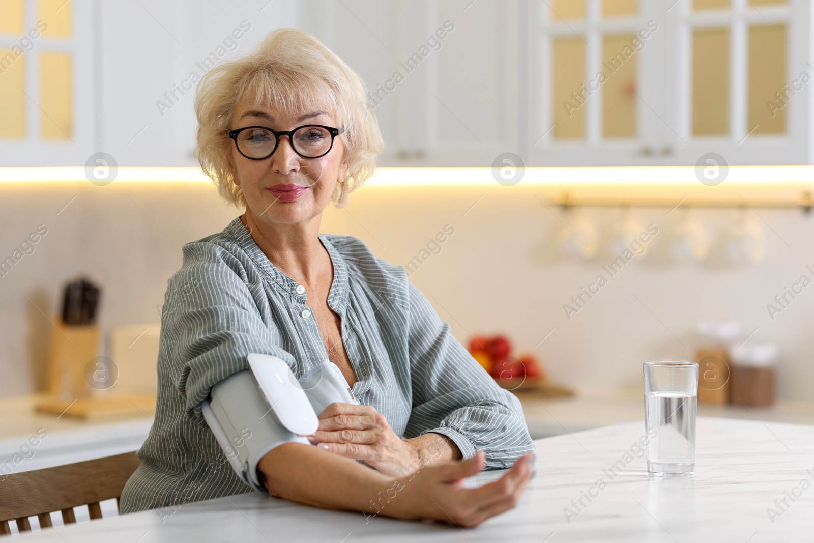 Photo of Senior woman measuring blood pressure at table in kitchen. Space for text