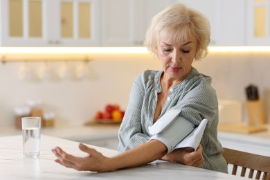 Photo of Senior woman measuring blood pressure at table in kitchen. Space for text