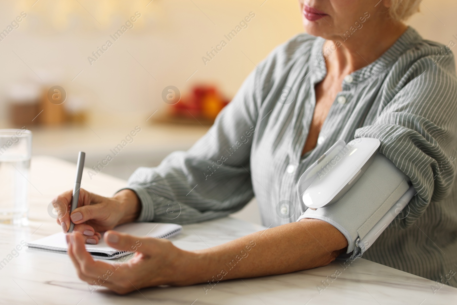 Photo of Senior woman writing results of blood pressure measurement in kitchen at home, closeup