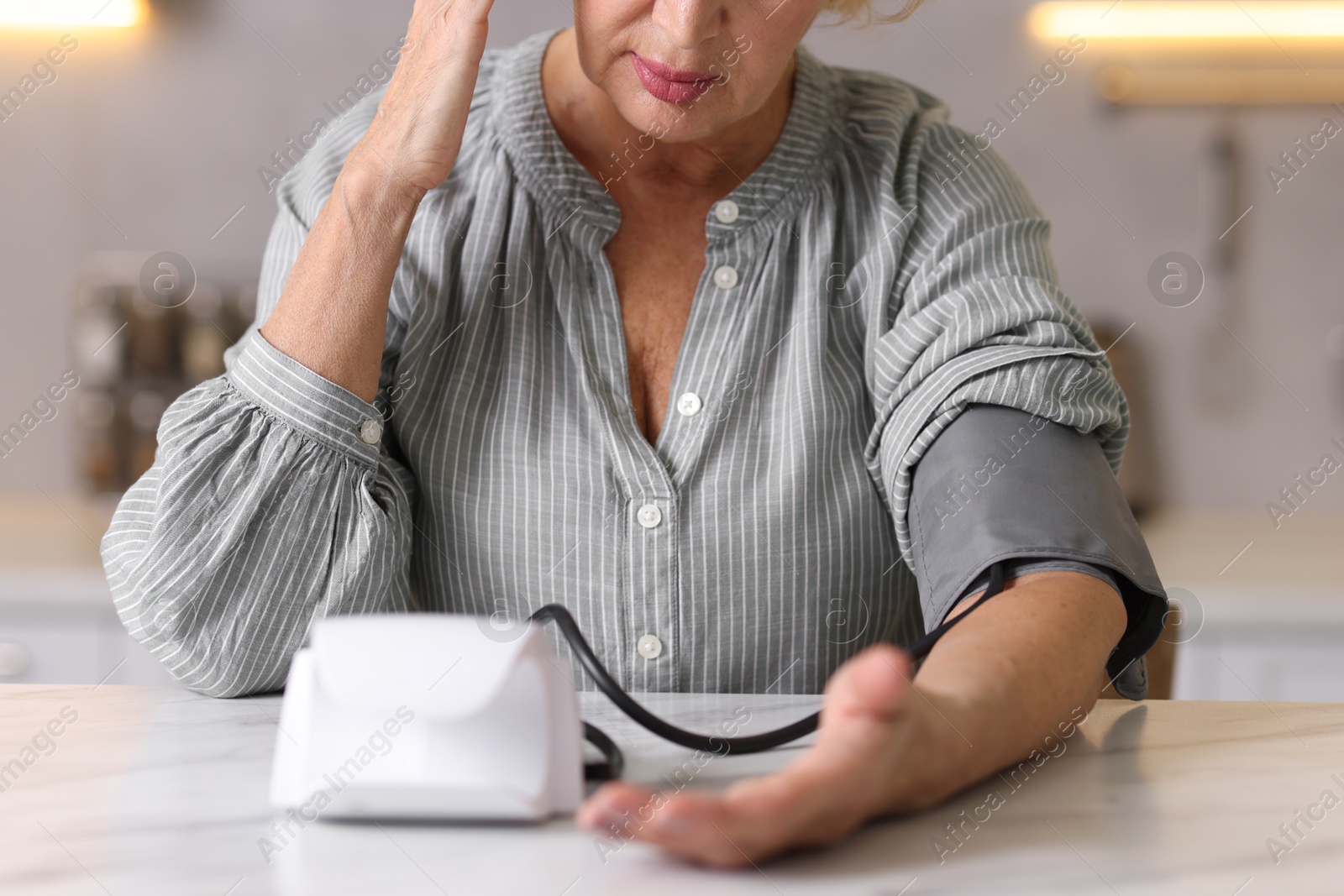 Photo of Senior woman measuring blood pressure at table in kitchen, closeup