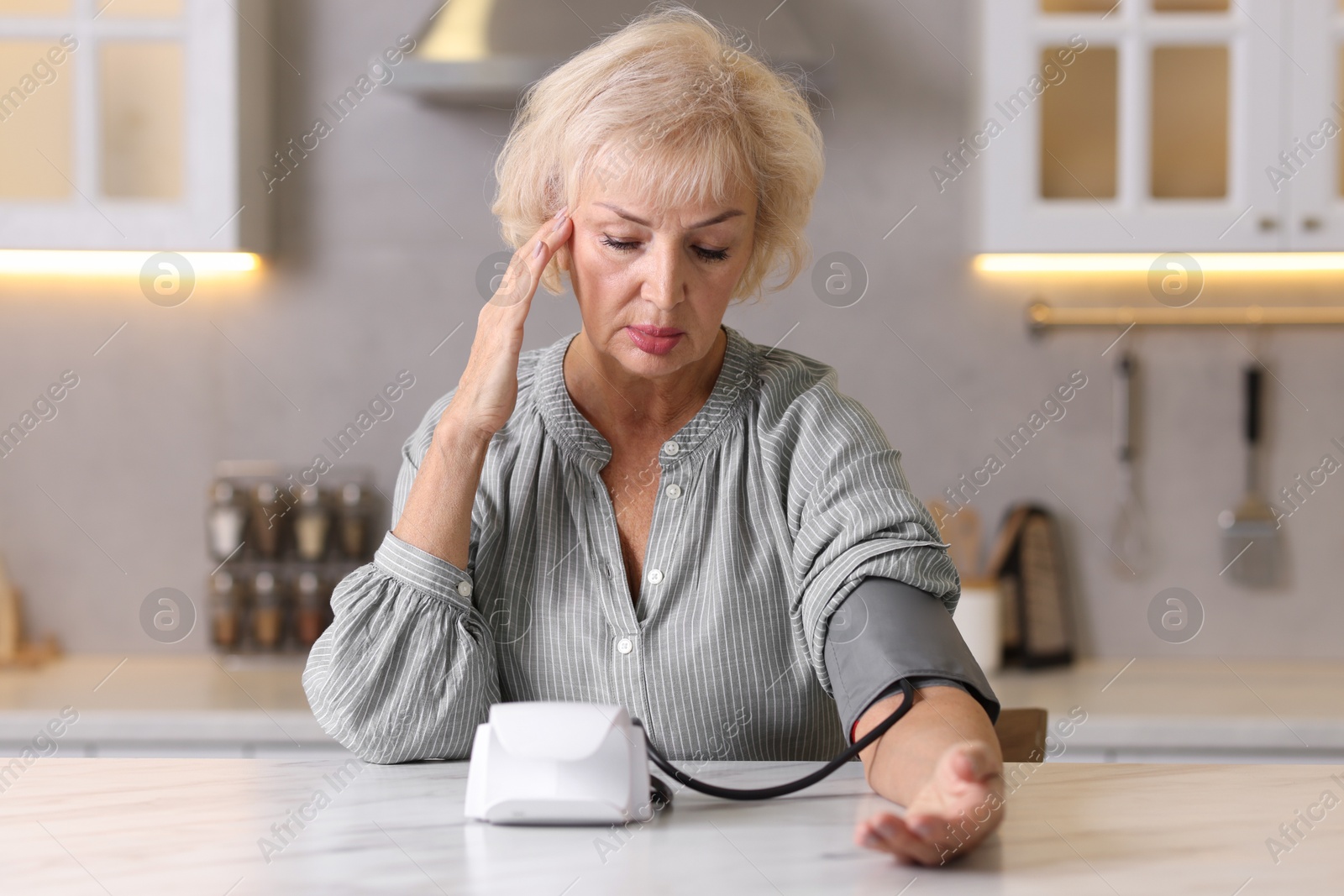 Photo of Senior woman measuring blood pressure at table in kitchen