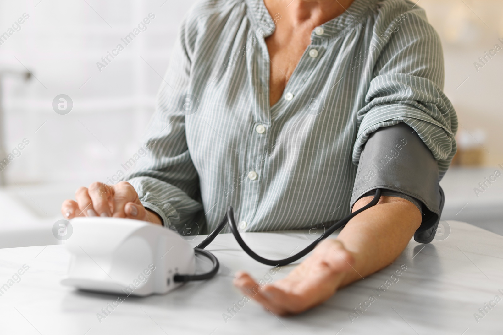 Photo of Senior woman measuring blood pressure at table in kitchen, closeup