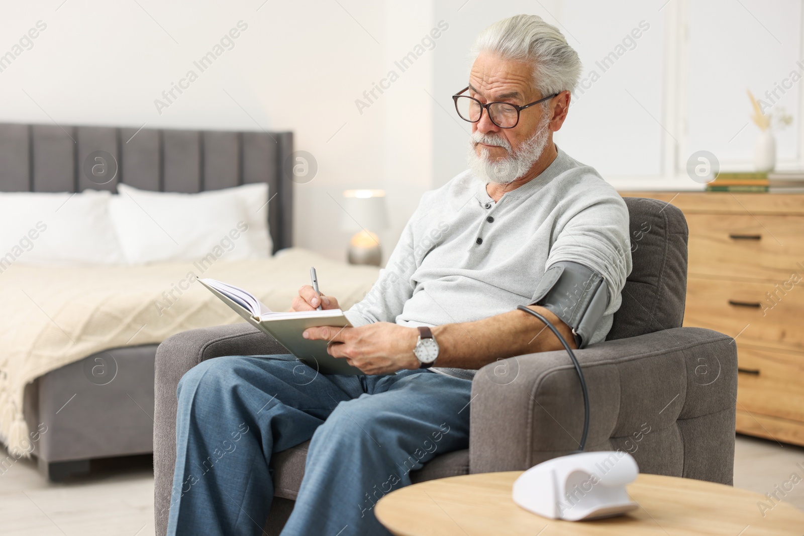 Photo of Senior man writing results of blood pressure measurement at home