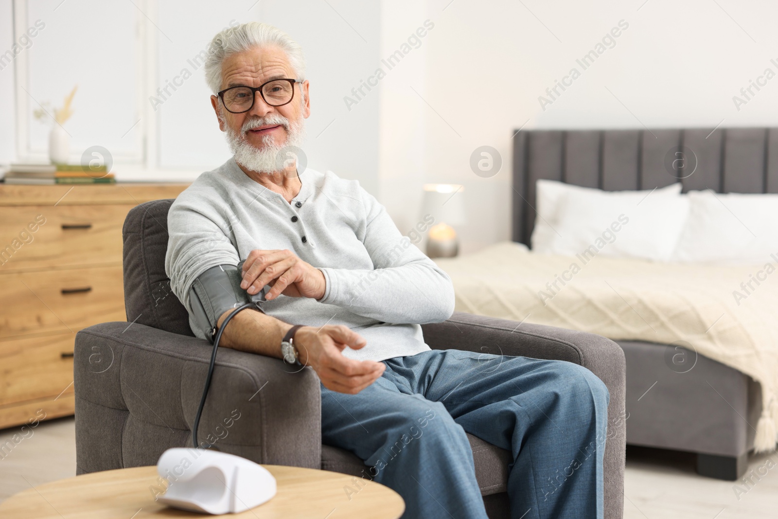 Photo of Senior man measuring blood pressure in armchair at home. Space for text