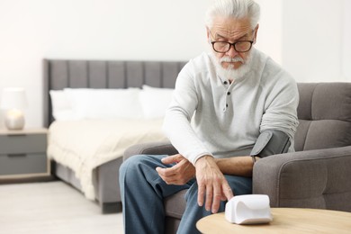 Photo of Senior man measuring blood pressure in armchair at home. Space for text