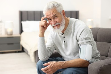 Photo of Senior man measuring blood pressure in armchair at home