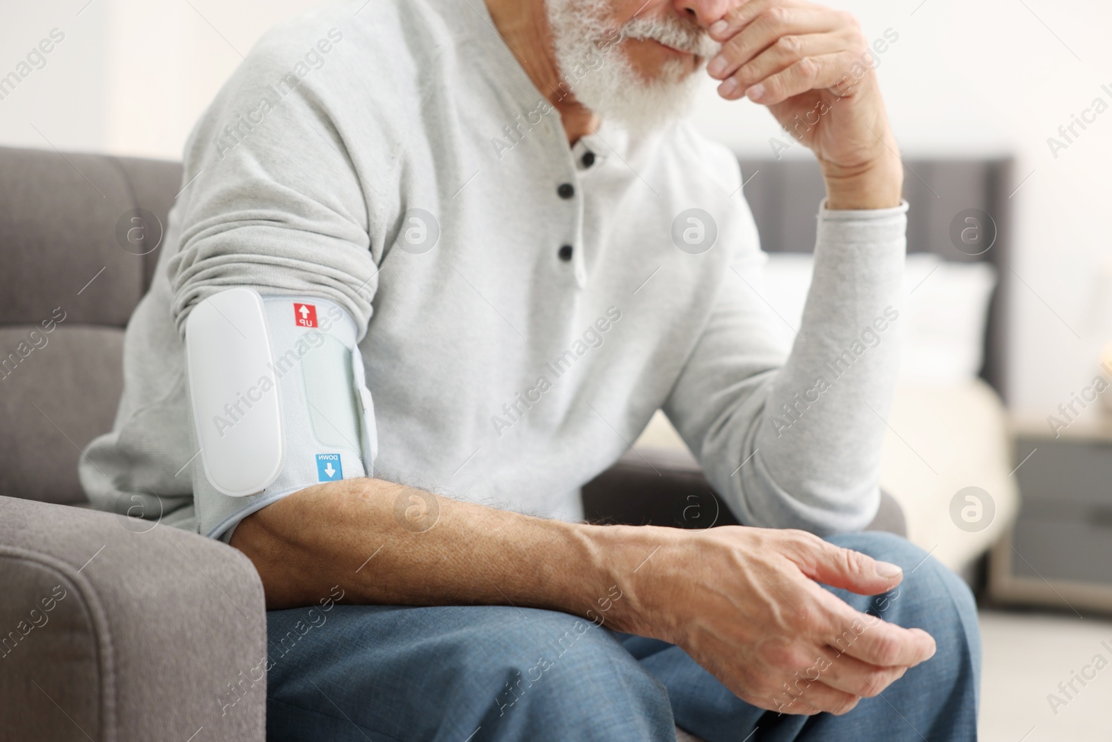 Photo of Senior man measuring blood pressure in armchair at home, closeup