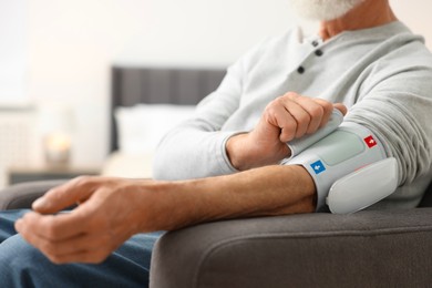 Photo of Senior man measuring blood pressure in armchair at home, closeup