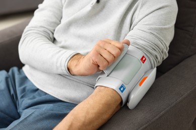 Photo of Senior man measuring blood pressure in armchair at home, closeup