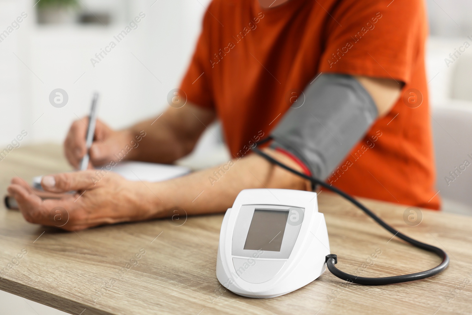 Photo of Senior man writing results of blood pressure measurement at table indoors, selective focus