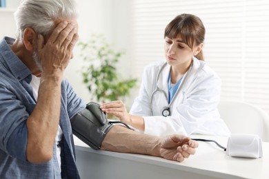 Photo of Doctor measuring senior man's blood pressure during appointment in hospital