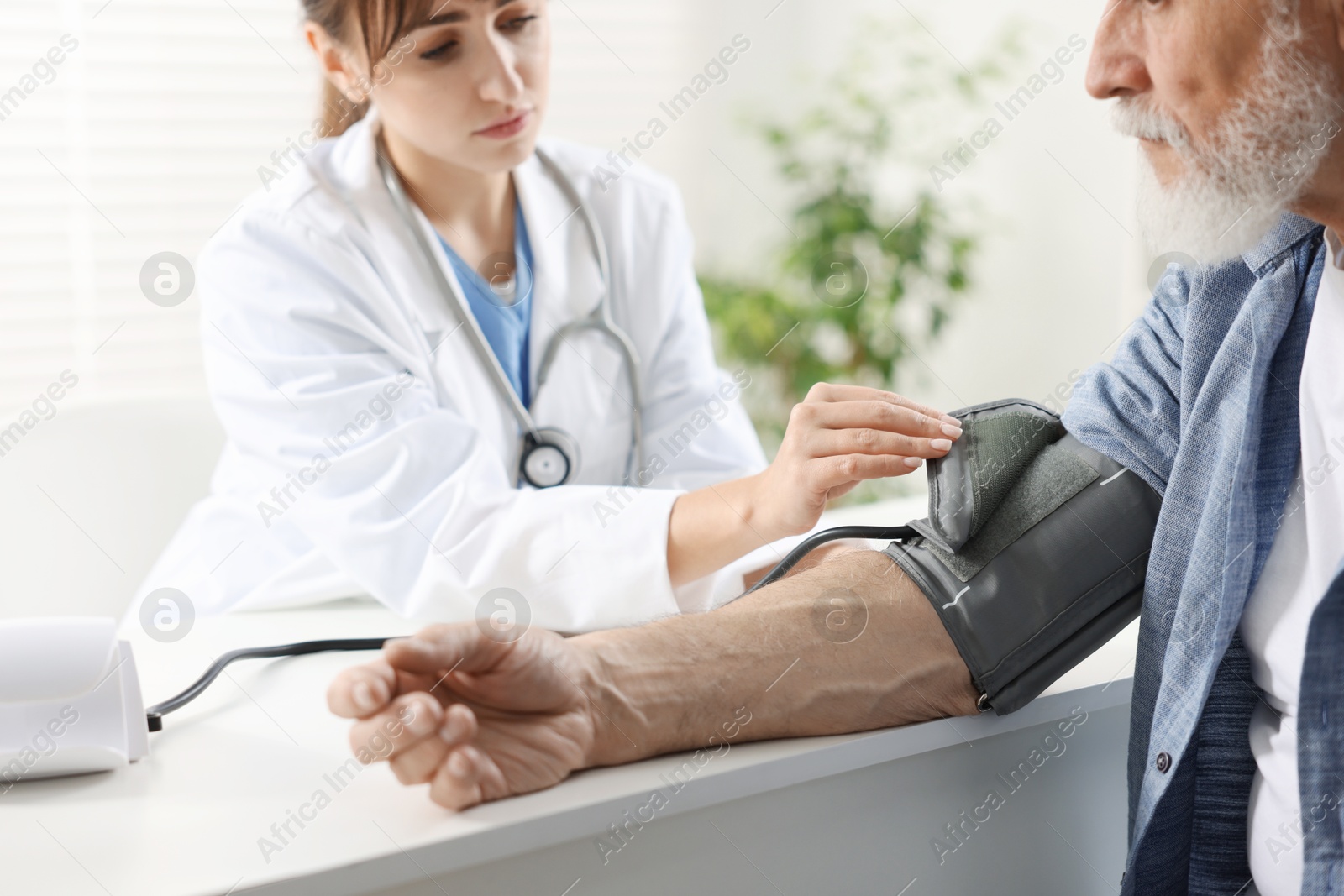 Photo of Doctor measuring senior man's blood pressure during appointment in hospital, closeup