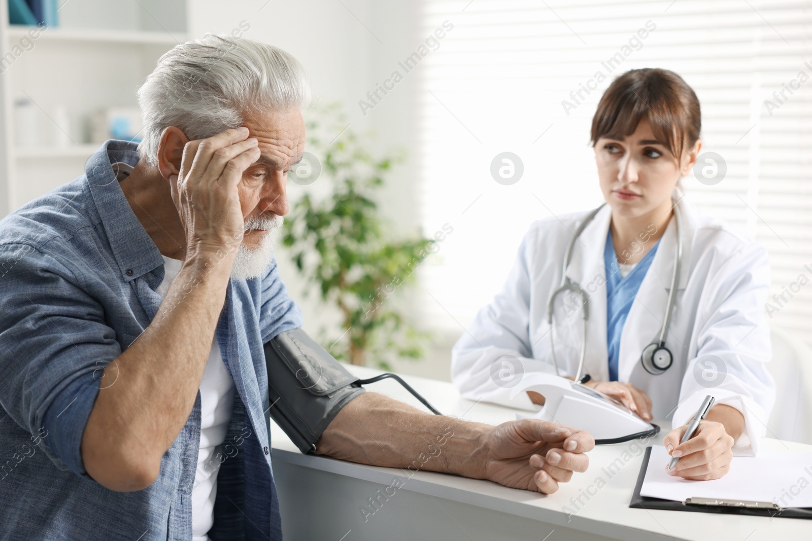 Photo of Doctor measuring senior man's blood pressure during appointment in hospital