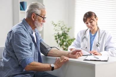 Photo of Doctor measuring senior man's blood pressure during appointment in hospital