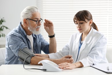 Photo of Doctor measuring senior man's blood pressure during appointment in hospital