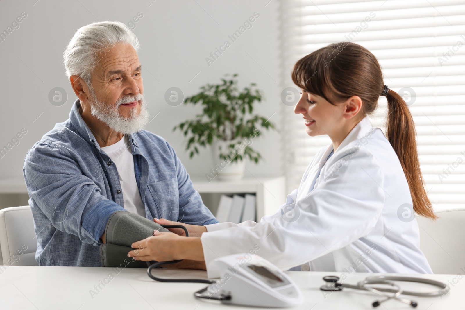 Photo of Doctor measuring senior man's blood pressure during appointment in hospital