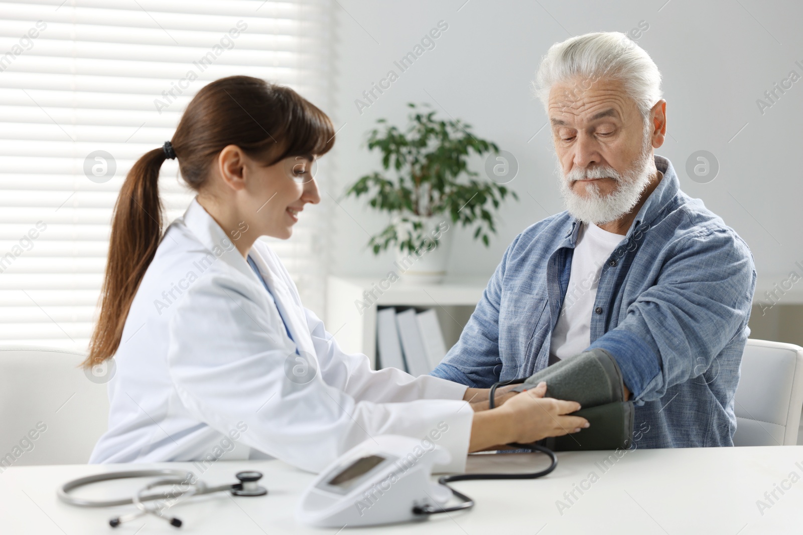 Photo of Doctor measuring senior man's blood pressure during appointment in hospital