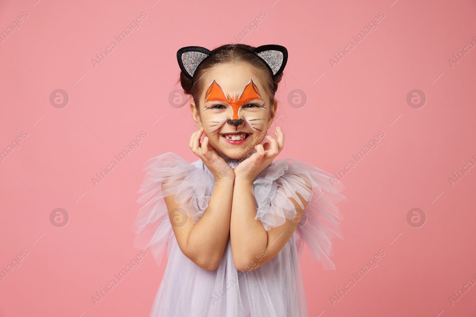 Photo of Cute girl with painted face and ears as cat on pink background