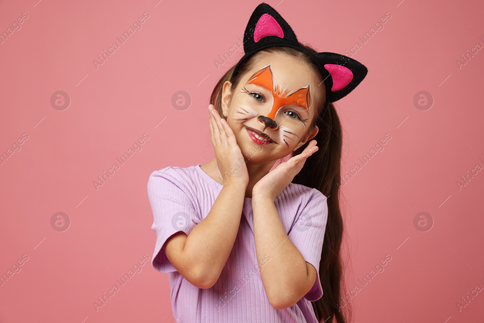 Photo of Cute girl with painted face and ears as cat on pink background